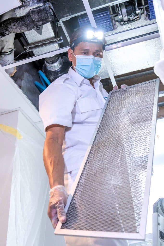 AC technician removing the AC filter from the AC unit in the gypsum ceiling