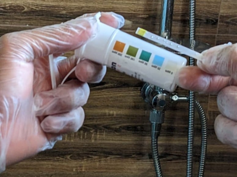 Technician performing a chlorine test on water coming out from a walk-in shower during a pipeline disinfection.