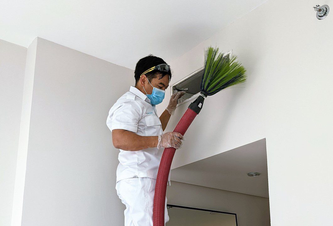 Air Conditioning technician holding the hose of the AC duct cleaning machine to perform AC duct cleaning
